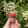 Love Spell Jar held in hand with red thread and Thurisaz rune, in front of elderflower – Mistwillow
