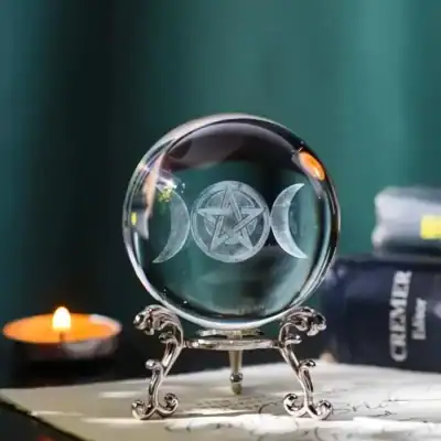 Crystal ball engraved with Triple Moon and pentacle symbol on an ornate silver stand, with candlelight and mystical ambiance in the background.