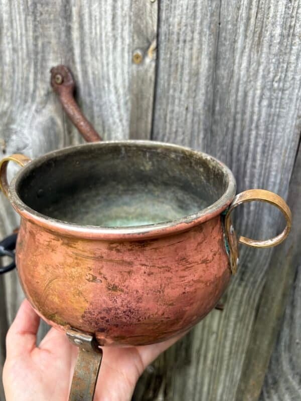 Close-up of an antique copper cauldron held by hand, showing its aged patina and weathered interior, perfect for witchcraft rituals and altar use.