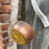 Vintage hammered copper cauldron with iron handle – held outdoors against rustic brick and wooden fence