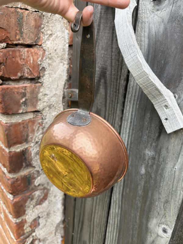Vintage hammered copper cauldron with iron handle – held outdoors against rustic brick and wooden fence