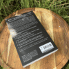 The back of the book "Witch" displaying text about its content and ISBN, lying on a wooden tray in the grass.