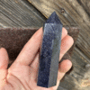 A hand holding a shimmering blue sandstone crystal tower, sparkling like a midnight sky against rustic wooden background.