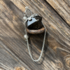 Obsidian-colored resin crystal pendulum with Tree of Life charm, resting on rustic wood and metal.