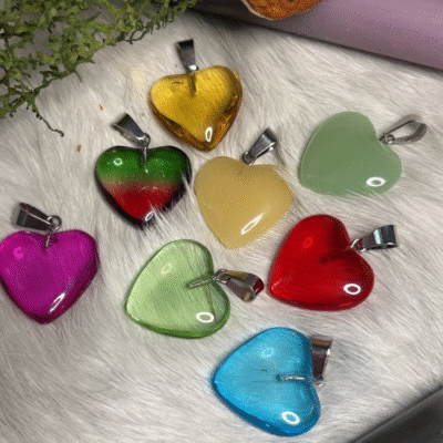 Colorful heart-shaped pendants in glass, displayed on white fur with moss and a candle – representing love, energy, and playfulness