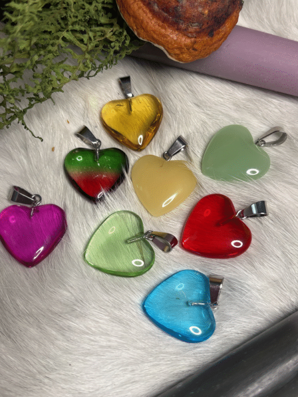 Colorful heart-shaped pendants in glass, displayed on white fur with moss and a candle – representing love, energy, and playfulness