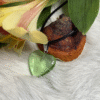 Transparent green heart pendant beside yellow flowers and natural mushroom on white fur