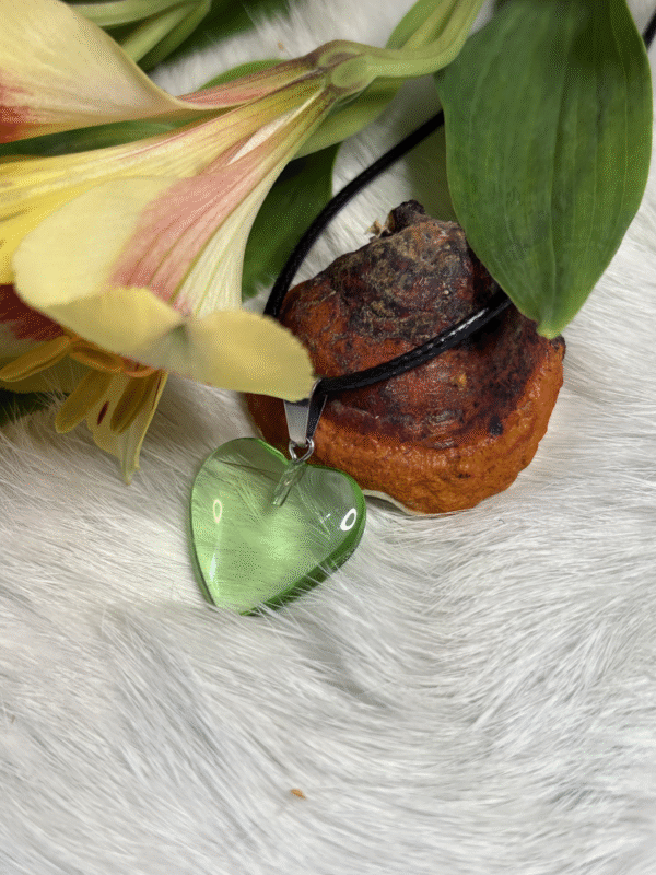 Transparent green heart pendant beside yellow flowers and natural mushroom on white fur