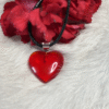 Red heart pendant on black cord, surrounded by red carnations on white fur
