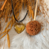 Transparent golden-yellow heart pendant with black cord, styled with dried oat stalks and a textured dried flower on soft white fur