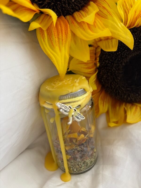 Glass jar filled with herbs and flowers, sealed with golden beeswax and adorned with a dragonfly charm, surrounded by vibrant sunflowers – a spell jar radiating joy, positivity, and solar magic.
