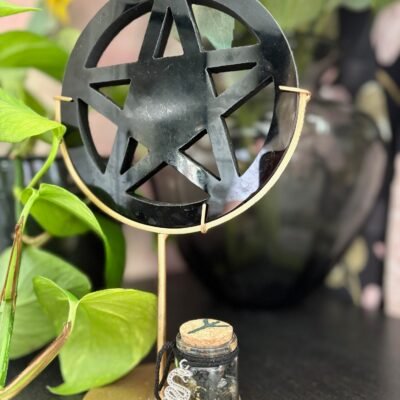 Black obsidian pentagram on golden stand with protective spell jar, adorned with a silver serpent charm.
