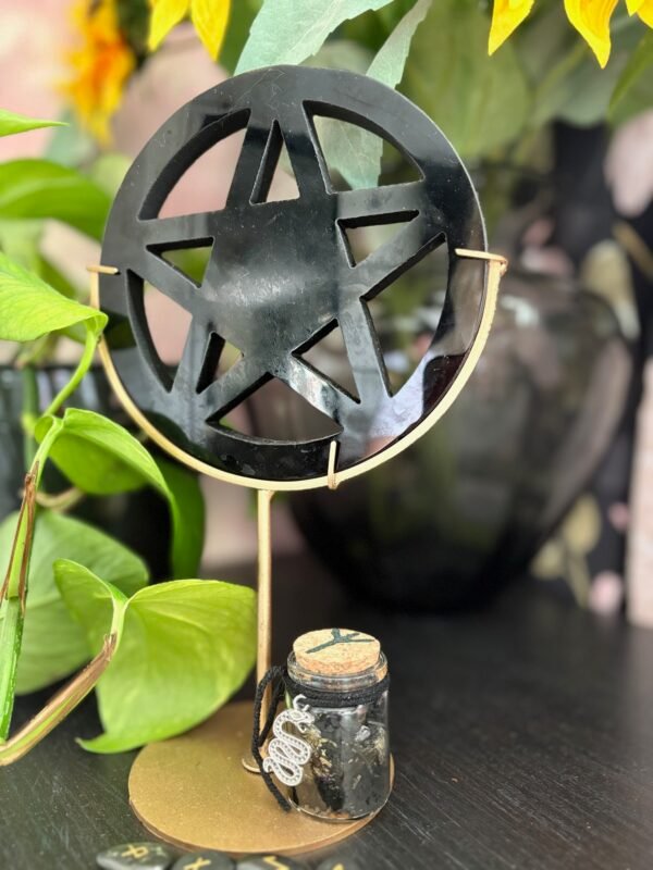 Black obsidian pentagram on golden stand with protective spell jar, adorned with a silver serpent charm.