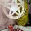 White quartz pentacle standing in golden frame with red intention jar and dried petals around.