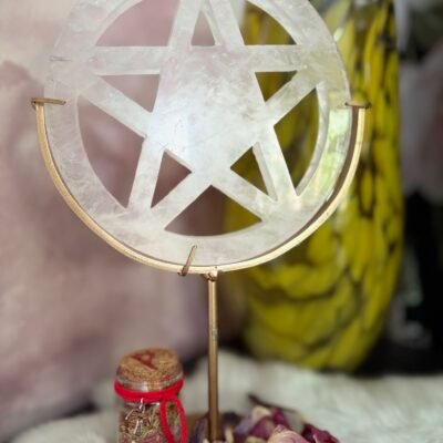 White quartz pentacle standing in golden frame with red intention jar and dried petals around.