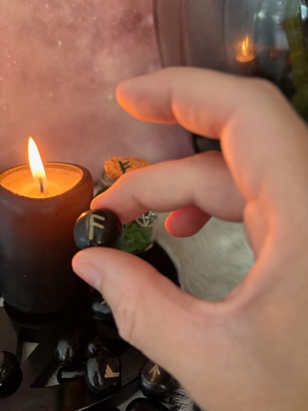 Black Obsidian rune stones with gold-etched Elder Futhark symbols, placed next to candle and spell jar on a soft ritual cloth