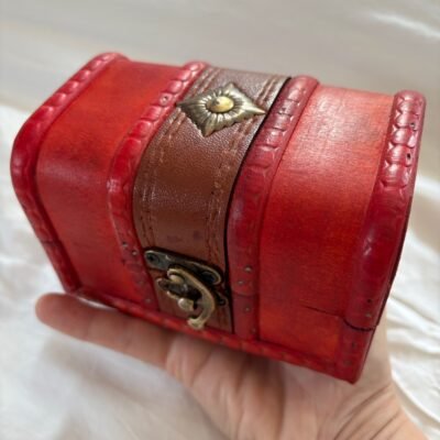 A small red wooden chest with brass clasp, shown open and closed, styled with a candle, runes, and witchy decor.