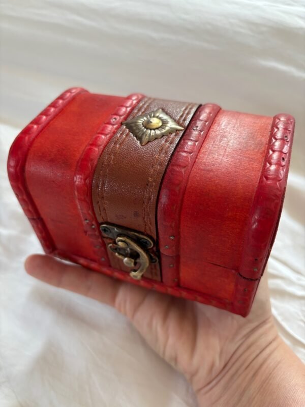 A small red wooden chest with brass clasp, shown open and closed, styled with a candle, runes, and witchy decor.