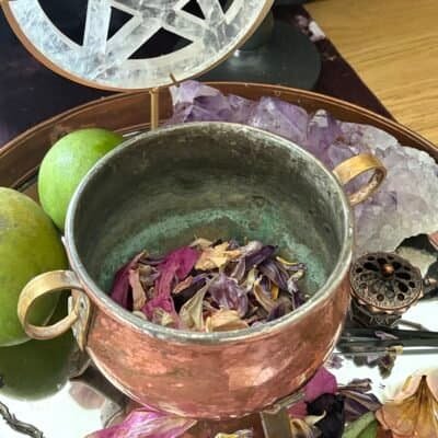 Mystical altar scene with a copper cauldron, selenite pentacle, candlelight, fruits, crystals, and dried petals – a sacred space for witchcraft rituals.