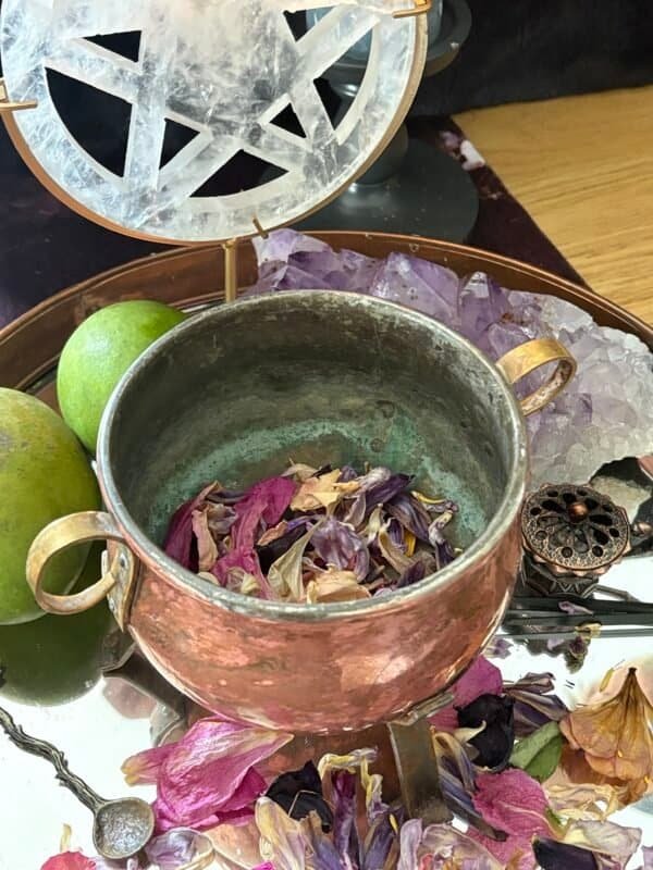 Mystical altar scene with a copper cauldron, selenite pentacle, candlelight, fruits, crystals, and dried petals – a sacred space for witchcraft rituals.