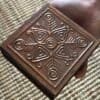 Hand holding an antique wooden altar box with embossed Nordic-style symbols, showing its compact size.