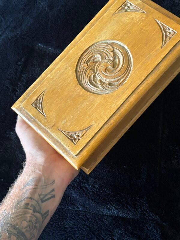 Hand holding vintage carved wooden box with swirling design.