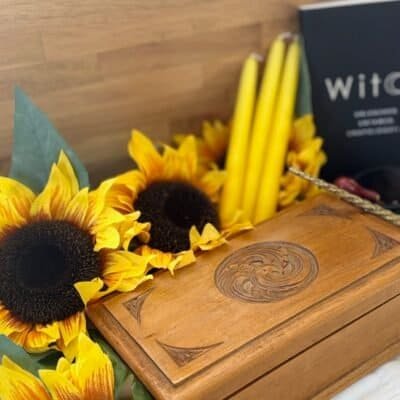 A handcrafted wooden witchcraft storage box surrounded by sunflowers, yellow candles, and a witchcraft book – perfect for tarot cards, crystals, and altar tools.