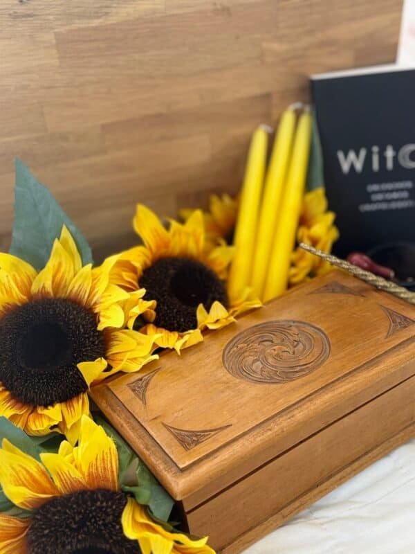 A handcrafted wooden witchcraft storage box surrounded by sunflowers, yellow candles, and a witchcraft book – perfect for tarot cards, crystals, and altar tools.