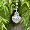 Amethyst-colored resin crystal pendulum with Tree of Life charm, hanging in front of lush green bamboo.