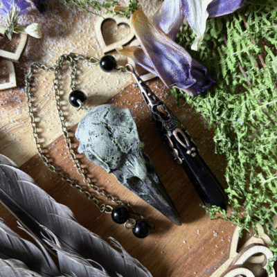 Obsidian crystal pendulum with raven skull detail, photographed against natural background, gothic witch style