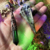 Obsidian crystal pendulum with raven skull detail, photographed against natural background, gothic witch style.
