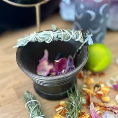 Antique cast iron cauldron on a mystical altar with herbs, petals, and a burning moon-phase candle in the background.