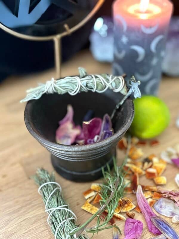 Antique cast iron cauldron on a mystical altar with herbs, petals, and a burning moon-phase candle in the background.