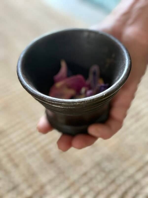 Hand holding a small antique cast iron cauldron, showcasing its size and aged texture.