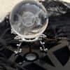Crystal ball engraved with Triple Moon and pentacle symbol on an ornate silver stand, with candlelight and mystical ambiance in the background.