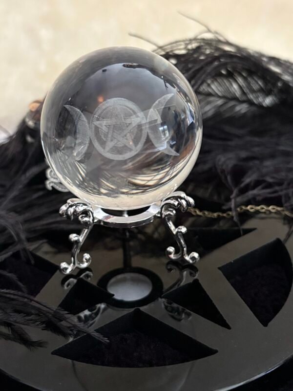 Crystal ball engraved with Triple Moon and pentacle symbol on an ornate silver stand, with candlelight and mystical ambiance in the background.