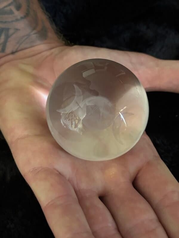 Crystal ball engraved with Triple Moon and pentacle symbol on an ornate silver stand, with candlelight and mystical ambiance in the background.