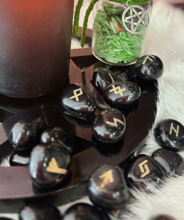 Black obsidian rune stones with golden symbols displayed in a magical setting beside a candle and spell jar.