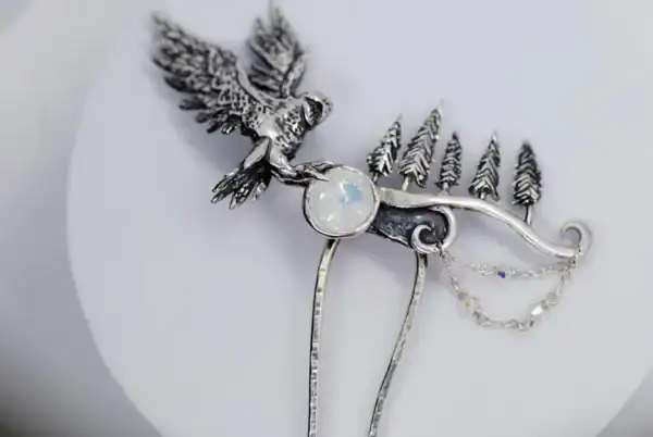 Close-up of a handcrafted silver hair comb with an owl and pine trees, featuring a glass opal stone, on a white background.