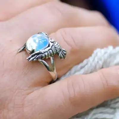 Close-up of owl silver ring with opal glass stone on hand, natural light glow.