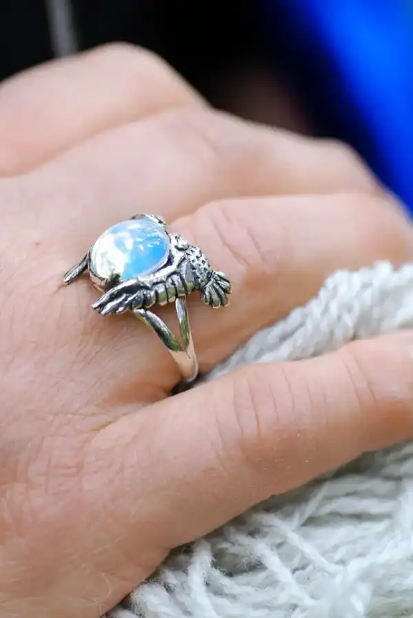 Close-up of owl silver ring with opal glass stone on hand, natural light glow.