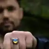 Man showing owl silver ring with opal glass on fist, blurred forest background.