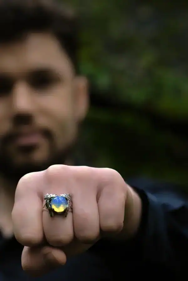 Man showing owl silver ring with opal glass on fist, blurred forest background.
