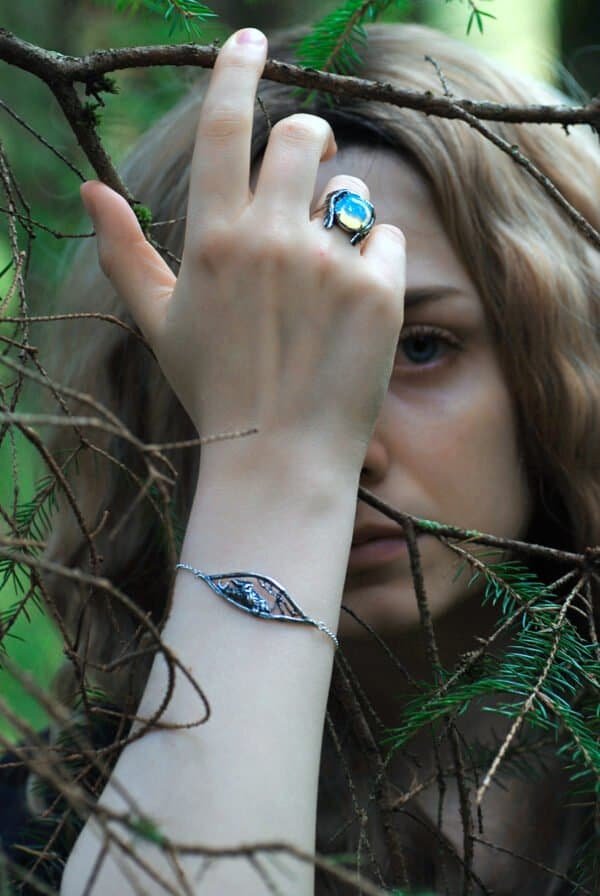 Nattuggla" silver bracelet worn in a mystical forest setting, paired with matching jewelry.