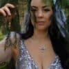 Woman wearing a handcrafted silver owl necklace with a glass opal, standing in a mystical forest setting.