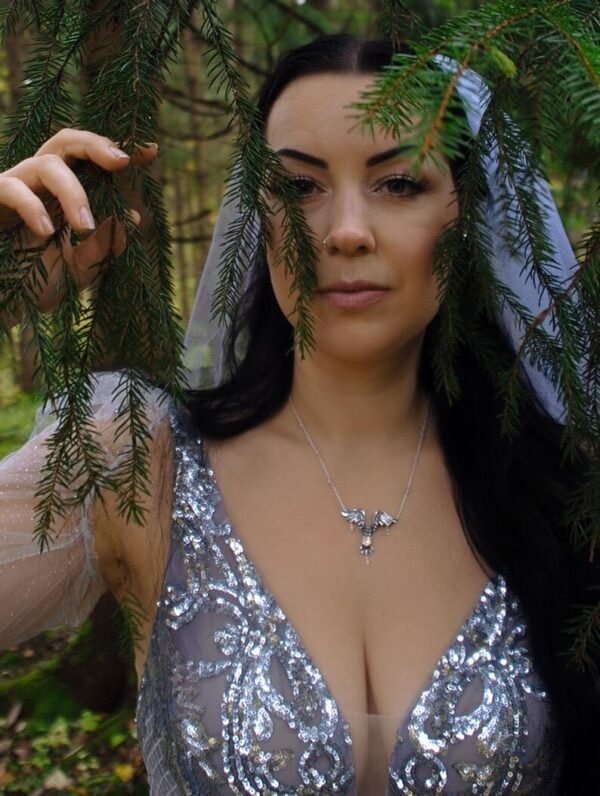 Woman wearing a handcrafted silver owl necklace with a glass opal, standing in a mystical forest setting.