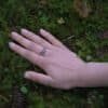 Hand resting on moss, showcasing the Diser silver ring in a natural forest setting.