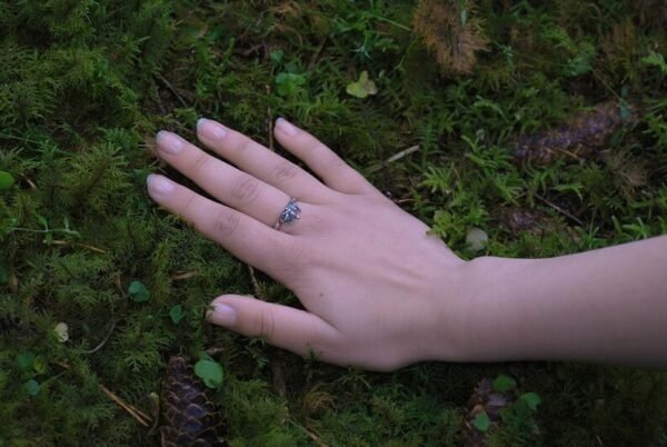 Hand resting on moss, showcasing the Diser silver ring in a natural forest setting.
