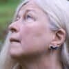 Older woman wearing silver owl earrings, inspired by Nordic mythology, looking upwards in nature.