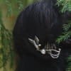 Woman wearing a silver owl hair comb with pine tree details, styled in dark hair among forest branches.